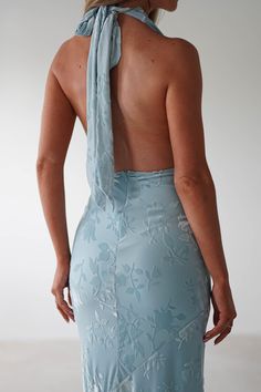 the back of a woman wearing a blue dress with an open neck and tie around her neck