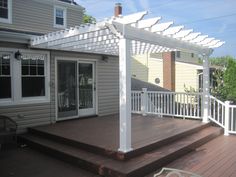 a white pergolan sitting on top of a wooden deck next to a house