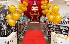 a red carpeted hallway with yellow balloons on the floor and hollywood themed walls behind it