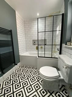 a white toilet sitting next to a bath tub in a bathroom with black and white tiles on the floor