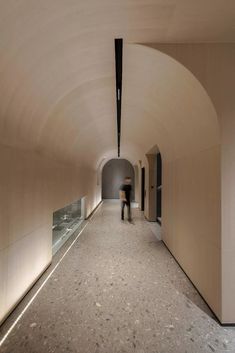 a person walking down a long hallway in a building with light colored walls and floors