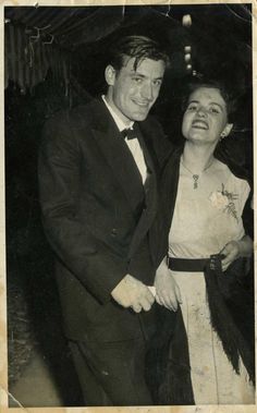 an old black and white photo of two people dressed in formal wear, one holding the other's hand