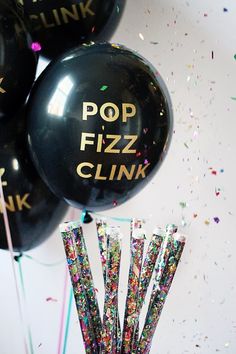 black balloons with pop fizz clink written on them and confetti sticks