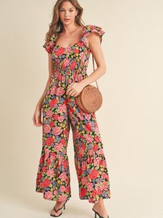 Let your confidence bloom in this flared ruffle hem jumpsuit. Sweetheart neckline and flutter sleeves add a touch of romance, while the tiered elastic waist panel accentuates your figure. Smocked back and pockets bring practicality. With a cut-out on the back, this black floral jumpsuit is a charming and functional choice. Color: Black Floral Fabric: 100% Cotton Brand: &Merci Sizes: S-M-L, Regular Sizing. Model is 5' 10.5" 32-24-36 and wears a S Casual Ruffled Jumpsuits And Rompers, Casual Fitted Jumpsuits And Rompers With Ruffle Hem, Casual Summer Jumpsuit With Flutter Sleeves, Casual Jumpsuits And Rompers With Ruffle Hem For Vacation, Summer Flutter Sleeve Jumpsuits And Rompers With Ruffles, Summer Ruffled Jumpsuits And Rompers With Flutter Sleeves, Vacation Swimwear, Black Floral Jumpsuit, Swimwear Sets