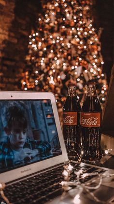 an open laptop computer sitting on top of a table next to a christmas tree with lights