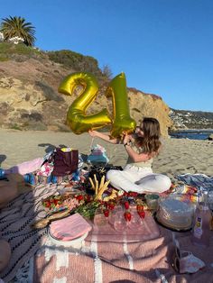 a woman is sitting on the beach with her number twenty two balloons in front of her