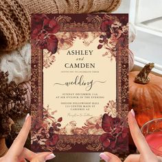 two hands holding up a wedding card in front of some pumpkins and other decorations