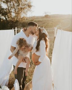 a man and woman kissing while holding a baby in front of clothes hanging on a line