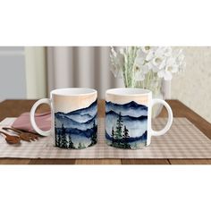 two coffee mugs sitting on top of a wooden table next to a vase with flowers