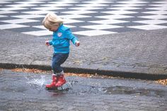 a little boy that is standing in the rain with red boots and water splashing on his feet