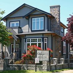 a gray house with red flowers in the front yard and a sign that says cottage