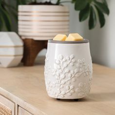 a white vase with two pieces of butter on it sitting on a table next to a potted plant