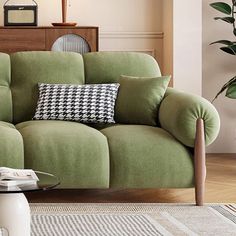 a living room with a green couch and coffee table in front of the couch is a potted plant