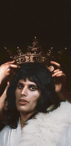 a man with a crown on his head in front of a black background and white fur