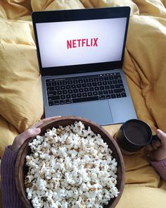 a person is holding a bowl of popcorn while using a laptop computer on their lap