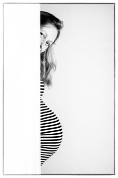 black and white photograph of a pregnant woman peeking out from behind a wall with her hands on her hips