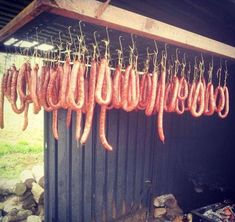 several sausages hanging from a grill in front of a building with rocks and grass