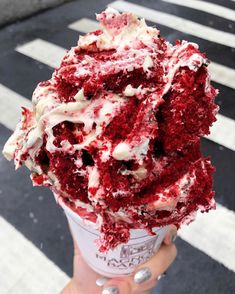 a person holding up an ice cream cone with red velvet and white frosting on it