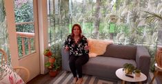 a woman sitting on top of a couch in a living room next to a window