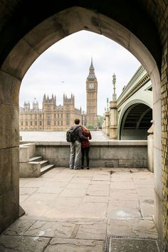 two people standing in an archway looking at the big ben clock tower