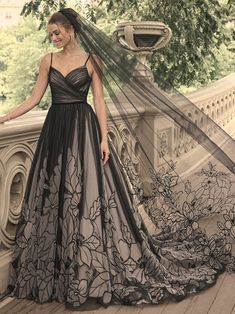 a woman standing on a bridge wearing a black and grey wedding dress with floral appliques