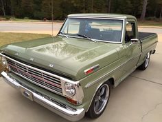 an old green pickup truck parked in a driveway