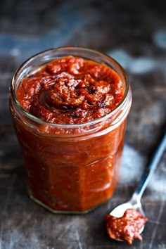 a jar filled with sauce sitting on top of a wooden table next to a spoon