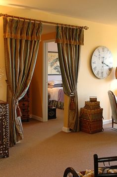 a bedroom with a clock on the wall and drapes open to reveal a bed