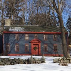 a red and blue house in the snow with rocks around it's base, surrounded by trees