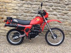 a red dirt bike parked in front of a stone wall with no wheels on it