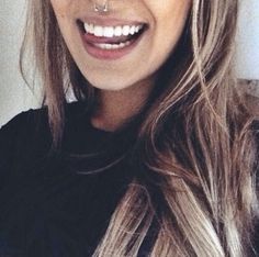 a close up of a person wearing a nose ring and smiling at the camera with long blonde hair