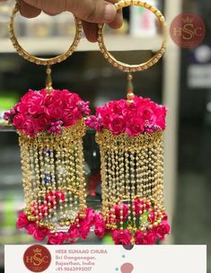 a person holding up some pink flowers in front of two gold hoop earrings with pearls hanging from them