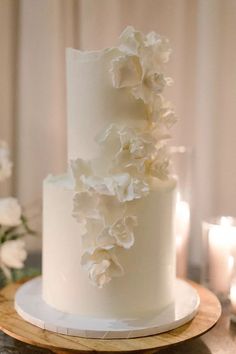 a wedding cake with white flowers on top is sitting on a table in front of candles