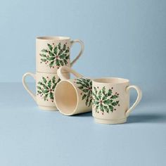 three mugs with holly designs on them sitting next to each other in front of a blue background