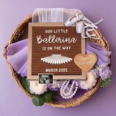 a basket filled with purple and white flowers next to a sign that says our little ballerina is on the way