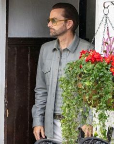 a man standing next to a potted plant in front of a door with sunglasses on