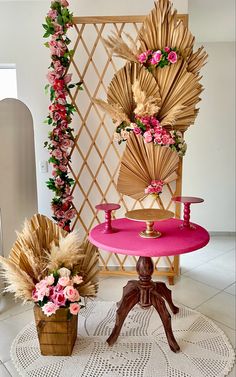 a pink table with flowers on it next to a wooden chair and potted plant