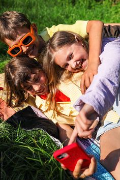 three children are laying on the grass and looking at a cell phone that is being held by their mother