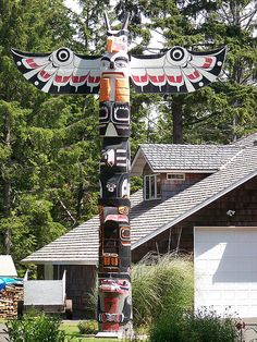 a totem pole in front of a house with two birds on it's head