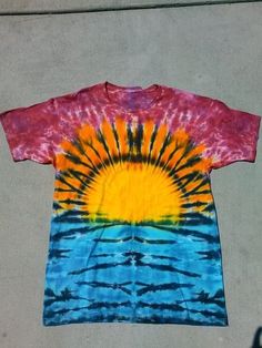 a tie - dyed t - shirt with the sun on it is laying on concrete