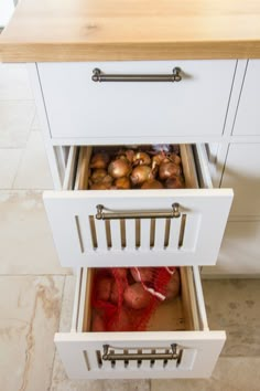 an open drawer in a kitchen filled with onions and other food items next to a counter top