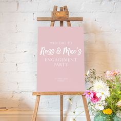 a pink sign sitting on top of a wooden easel next to flowers and vases