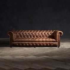 a brown leather couch sitting on top of a wooden floor next to a black wall