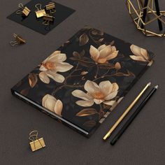 an open notebook with flowers on it next to some pens and other items that are laying around