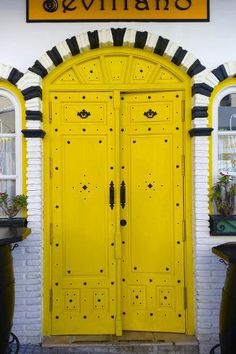 a yellow door is in front of a white brick building with potted plants on either side