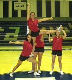 four girls in red shirts and black shorts are standing on a basketball court with their arms up