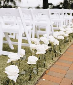 rows of white chairs lined up in the grass with flowers on each chair and brick walkway