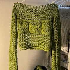 a green crocheted sweater hanging on a clothes rack next to a pair of shoes