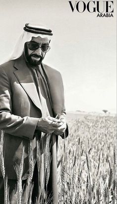 a black and white photo of a man in a suit standing in a wheat field