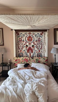 a person laying in bed under a white comforter with an intricate tapestry on the wall